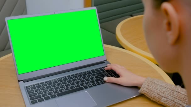 Vrouw op zoek naar laptop computer met blanco groen scherm in cafe - Video