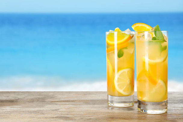 Glasses of citrus refreshing drink on wooden table near sea, space for text - Foto, Bild