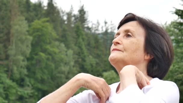 Senior vrouw doet een stretching oefening voor de bovenarmen buiten over landschap van bos en bergen - Video