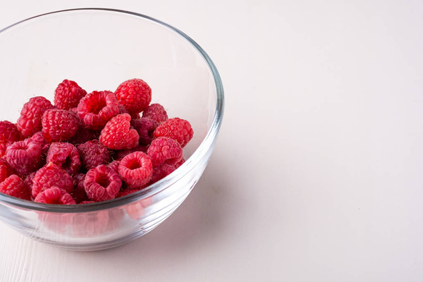 Raspberry red berries in transparent glass bowl plate tasty sweet bright on white background copy space macro - Photo, Image