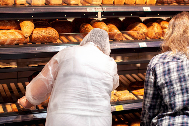 woman seller put fresh bread at bakery store shelf. - Photo, Image