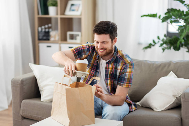 smiling man unpacking takeaway food at home - Foto, Bild