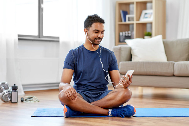 indian man with smartphone on exercise mat at home - Foto, Bild