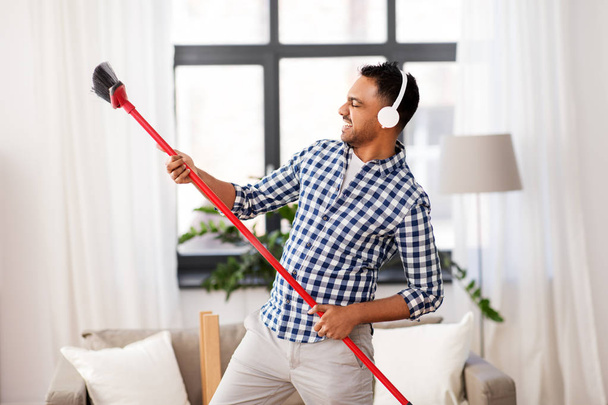 man with broom cleaning and having fun at home - Photo, Image