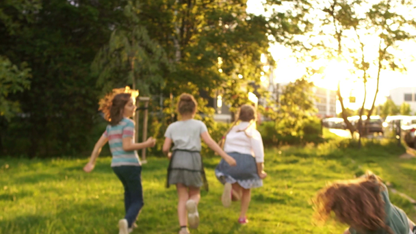 Παιδιά μαθητές που τρέχουν στην απόσταση στο φόντο των πράσινων δέντρων και του ηλιοβασιλέματος. Το αγόρι κάνει μια τούμπα στα χέρια του. Σχολική φιλία, επιστροφή στο σχολείο, φλόγα του φακού - Πλάνα, βίντεο