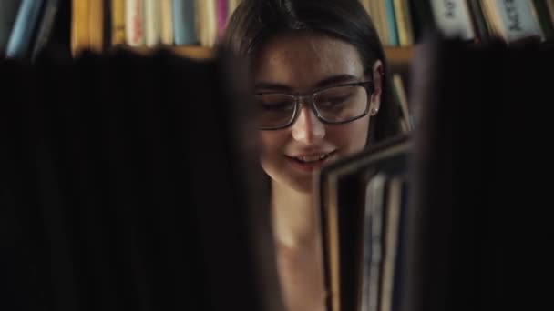 Atractiva joven buscando un libro de una estantería en la biblioteca
 - Imágenes, Vídeo