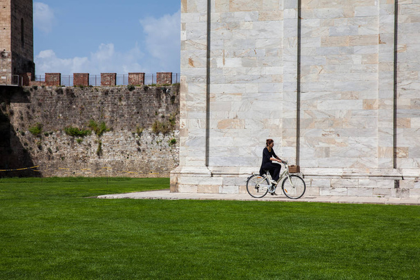 Woman biking next to the ancient walls of Pisa and Monumental Cemetery at the Square of Miracles in a beautiful early spring day - Photo, image