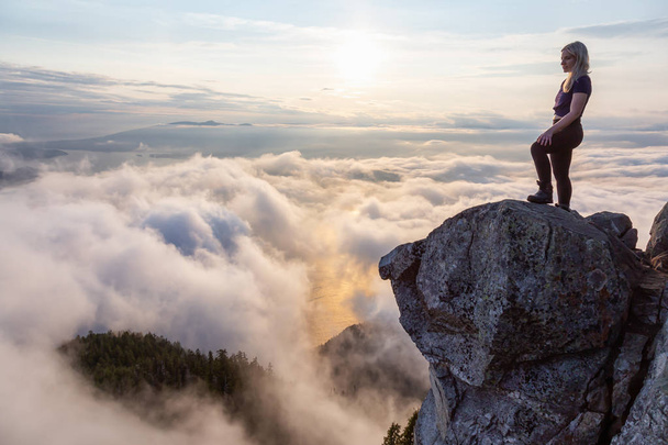 Awanturnika kobieta Hiker na szczycie góry pokryte chmurami podczas tętniącego życiem letniego zachodu słońca. Podjęte na szczycie St Mark's Summit, West Vancouver, Kolumbia Brytyjska, Kanada. - Zdjęcie, obraz