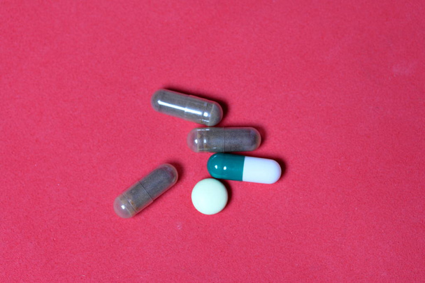 Gelatin pills and tablets of different colors. Medicines scattered on the background of coral color. - Foto, Bild