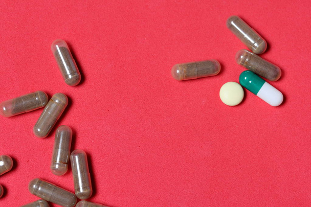 Gelatin pills and tablets of different colors. Medicines scattered on the background of coral color. - Photo, Image