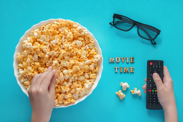 Hands holds popcorn and TV remote, bowl of popcorn and 3D glasse - Foto, immagini