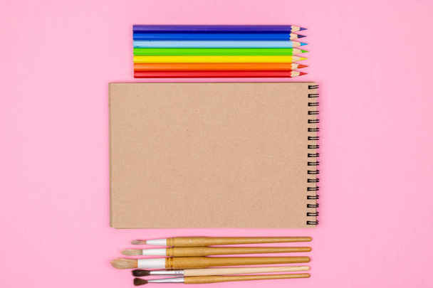 Watercolour brushes, Coloured pencils, notebook isolated on pink background for mockup. Flat lay, top view. Concept: back to school. - Fotó, kép