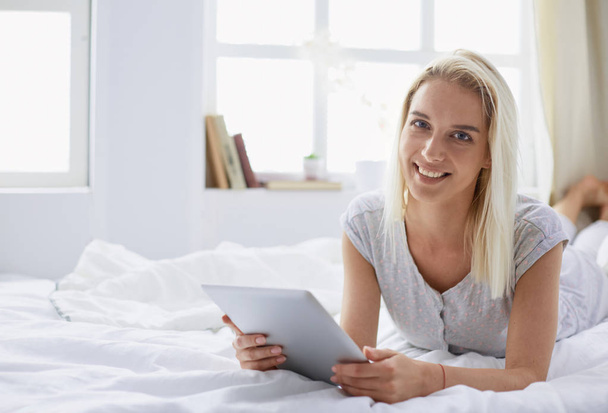 Girl holding digital tablet with blank screen and smiling at camera in bedroom - Foto, afbeelding