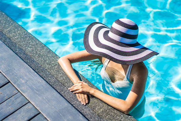 Seyahat için yüzme havuzunda şapkalı güzel genç Asyalı kadın - Fotoğraf, Görsel