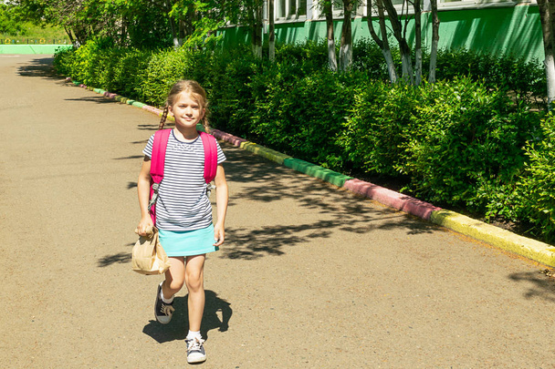 Маленька дівчинка з рожевим рюкзаком і паперовим пакетом з укусом ходить до школи. Шкільна концепція. Горизонтальна рамка
. - Фото, зображення