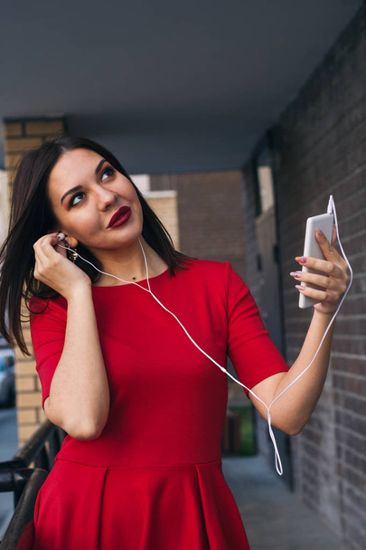 belle jeune femme avec rouge à lèvres rouge en robe rouge utilise téléphone et écouteurs
 - Photo, image