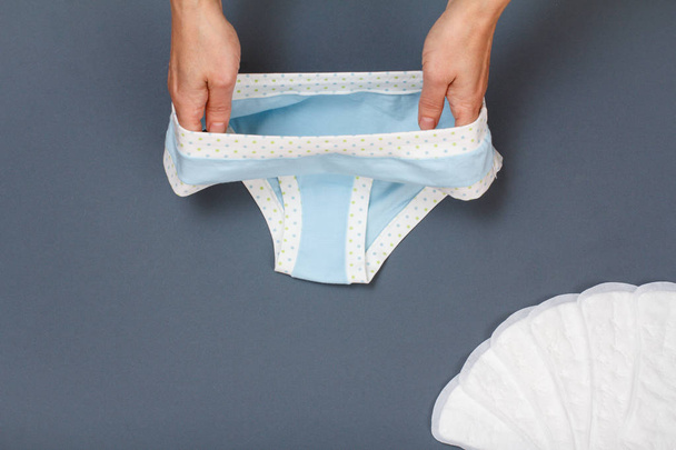 Women's hands with beautiful panties and sanitary pads on gray background. - 写真・画像