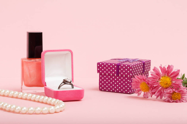 Caja con anillo, esmalte de uñas, caja de regalo y flores sobre fondo rosa
. - Foto, imagen