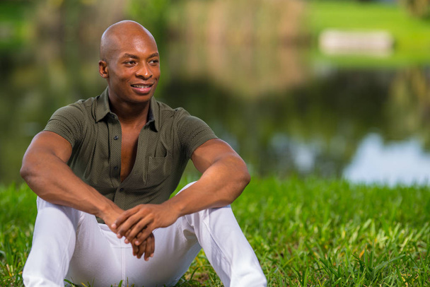 Muodikas afroamerikkalainen mies istuu nurmikolla.
  - Valokuva, kuva