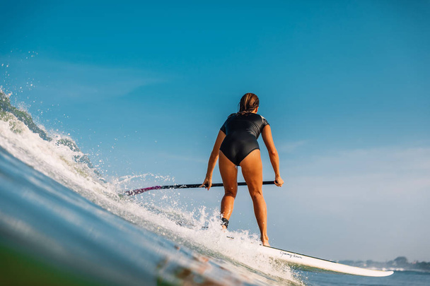 2019. április 12. Bali, Indonézia. Állj fel lapát surf lány lovagolni az óceán hullám. Állj fel lapát szörfözés Balin - Fotó, kép