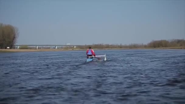 Achterste brede weergave van atleet Roeien op de rivier in een kano. Roeien, kanoën, peddelen. Opleiding. Kajakken. Man zeilen tegen de brug. - Video