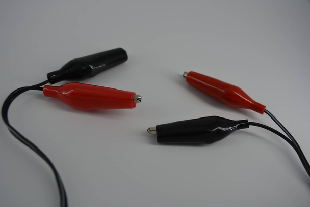 Ηλεκτρικό σύρμα με κόκκινο και μαύρο συνδετήρες για τη σύνδεση σε μια πηγή ενέργειας, συν και μείον από την πρίζα, μπαταρία. Μεταλλικές κροκόδειλοι σε ένα στενό ελαστικό κέλυφος για μια ασφαλή και άνετη ηλεκτρική σύνδεση. - Φωτογραφία, εικόνα