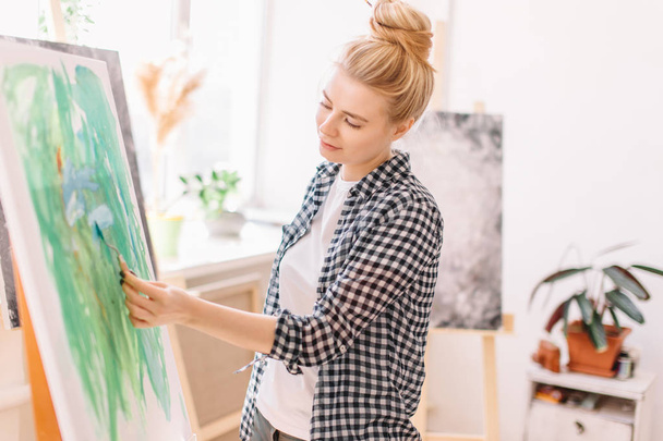 Female beautiful artist painting picture, using spatula in workshop - Фото, зображення