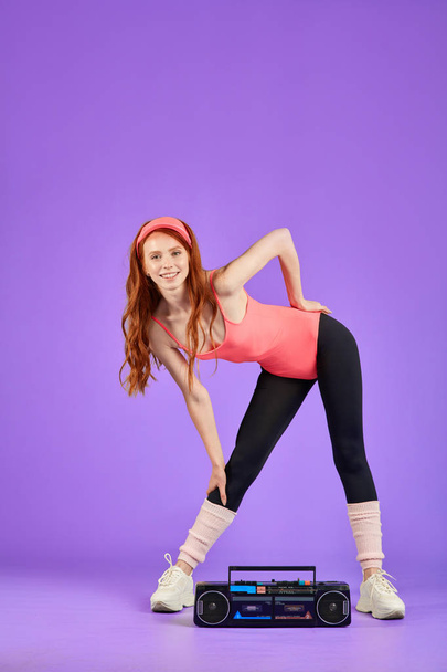 motivated slim girl doing stretching exercises, leans aside and listens to music - Foto, imagen