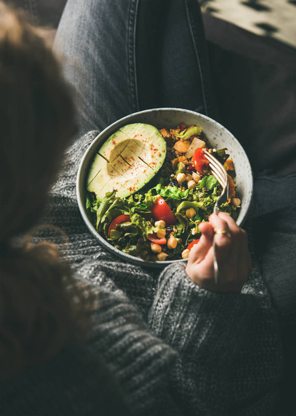Healthy vegetarian dinner. Woman in jeans and woolen sweater holding bowl with fresh salad, avocado, grains, beans, roasted vegetables, top view. Superfood, clean eating, vegan, dieting food concept - Foto, afbeelding