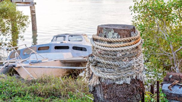Мотузка навколо старої дерев'яної пошти тримає мавританський човен
 - Фото, зображення