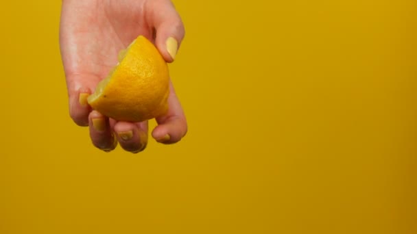 Θηλυκό χέρι με κίτρινο μανικιούρ συμπιέζει μισό λεμόνι σε κίτρινο φόντο - Πλάνα, βίντεο