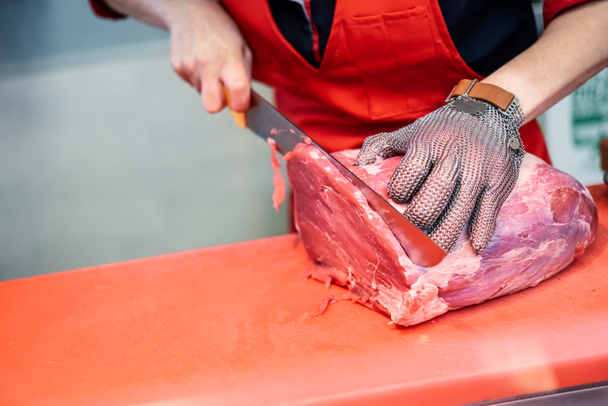 Nainen, joka leikkaa tuoretta lihaa lihakaupassa metalliverkolla
 - Valokuva, kuva