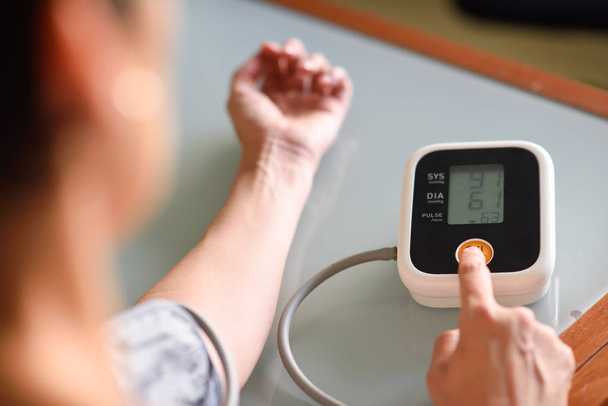 Nainen mittaamassa omaa verenpainettaan kotona
. - Valokuva, kuva