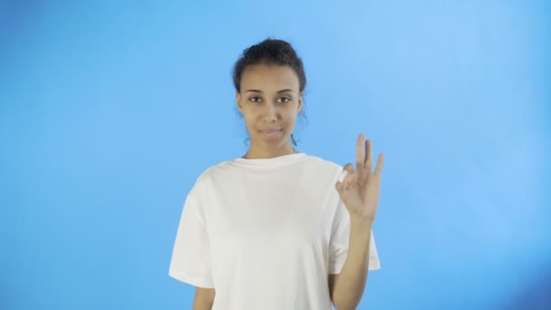 CuteAfro-American Girl is showing ok with two thumbs and smiling on Blue Background in Studio - Filmagem, Vídeo