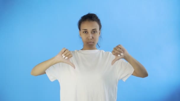 mooi jong meisje in een wit t-shirt toont duim naar beneden met beide handen op blauwe achtergrond - Video