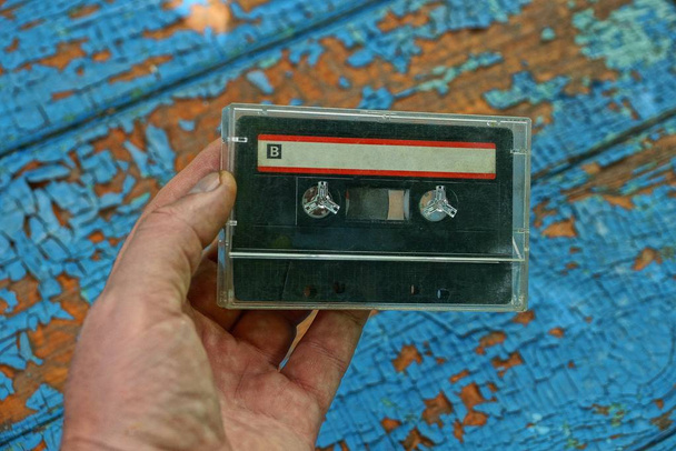 одна стара аудіокасета в прозорій коробці, лежить на руці на синьому фоні
 - Фото, зображення