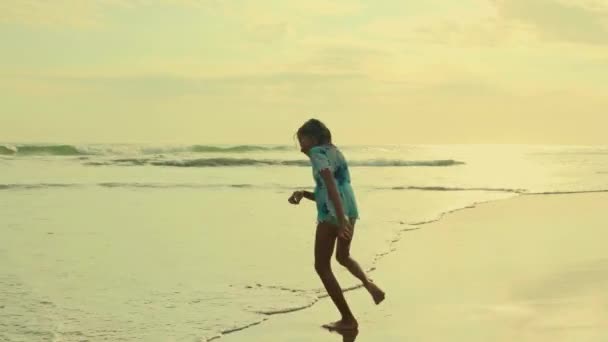 Gimbal стезіcam відстеження пострілу з 8 або 9 років красиві і щасливі азіатських Індонезійська дитини дівчина працює безтурботним на пляжі веселяться насолоджуючись літні канікули на захід сонця на екзотичному острові - Кадри, відео