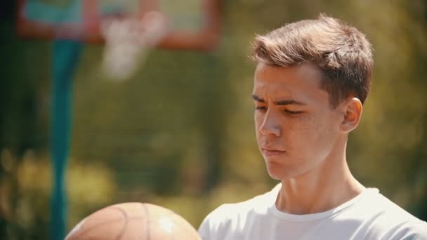 Un joven de pie en un campo de deportes y girando la pelota de baloncesto en su dedo
 - Metraje, vídeo