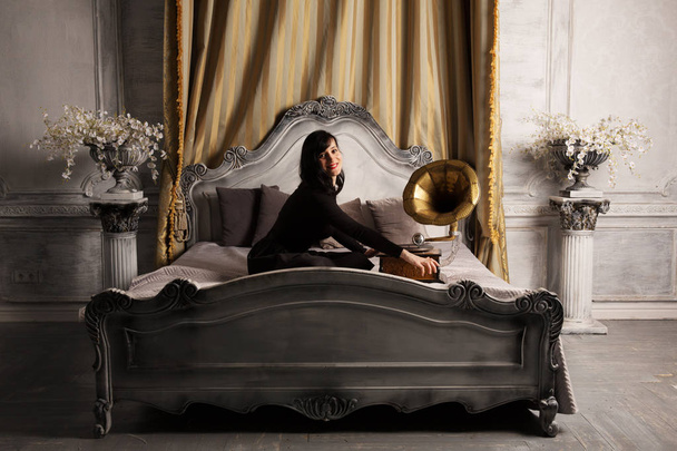 Muotokuva nuori kaunis nainen malli musta seksikäs mekko istuu sängyllä kanssa gramofoni sisustus studio
. - Valokuva, kuva