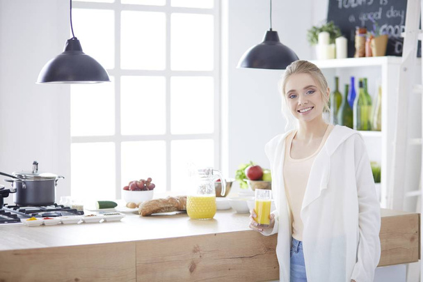 Attractive woman holding a glass of orange juice while standing in the kitchen - Foto, Bild