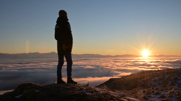 A sziluettje egy férfi áll naplemente felett a felhők, és szemléli a lenyugvó nap. A nyugalom és a kedvtelési célú utazás fogalma - Felvétel, videó