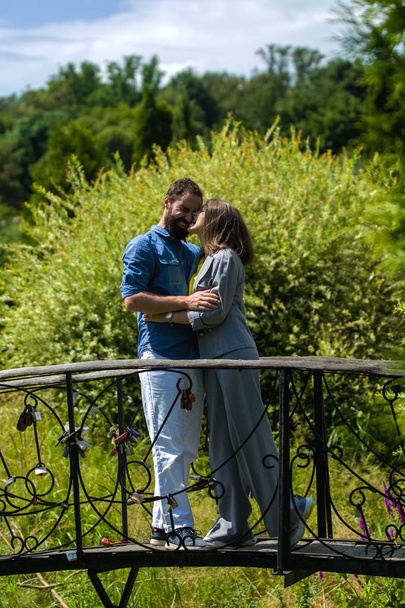 Joven y elegante pareja amorosa de pie y juega el tonto, diversión, abraza en el parque en el puente entre los verdes de verano
. - Foto, imagen