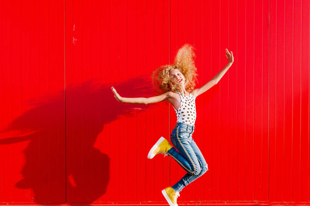 mooi tiener meisje maakt een sprong tegen de achtergrond van een rode muur - Foto, afbeelding