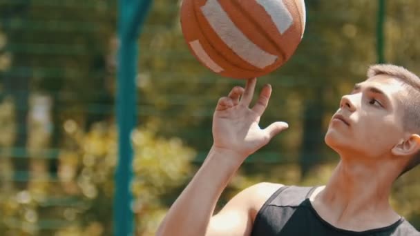 Un joven confiado de pie en un campo de deportes y girando la pelota de baloncesto en su dedo
 - Metraje, vídeo