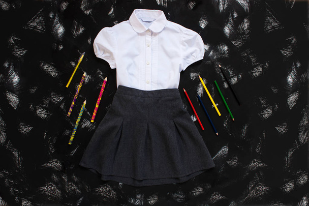Camisa blanca, falda gris y artículos de papelería sobre fondo negro. El primero de septiembre, nuevo año escolar
. - Foto, imagen