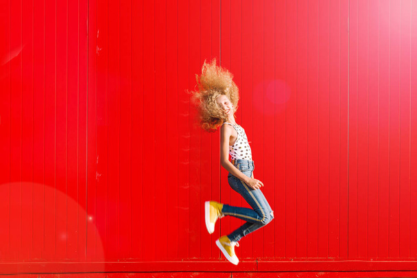 красива дівчина-підліток робить стрибок на тлі червоної стіни
 - Фото, зображення