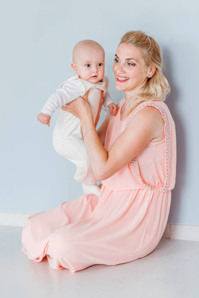 η μητέρα με ένα ροζ φόρεμα κρατά ένα μικρό γιο στην αγκαλιά της και χαμογελάει - Φωτογραφία, εικόνα