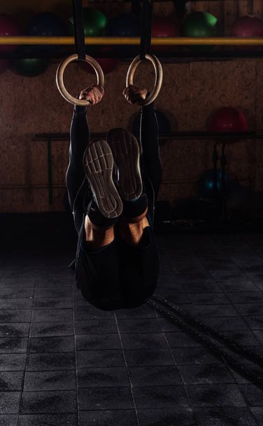 Молодой спортсмен подтягивается к гимнастическим кольцам
 - Фото, изображение