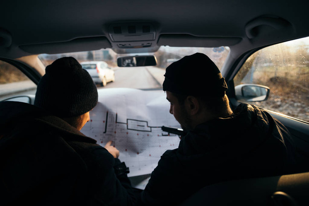 Двое грабителей, планируя и указывая на синюю ленту (карту) своего автомобиля
 - Фото, изображение