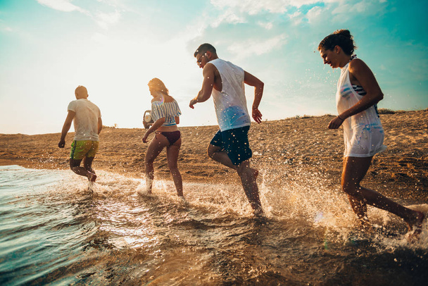 Grupo de amigos felices corriendo al agua al atardecer
 - Foto, Imagen